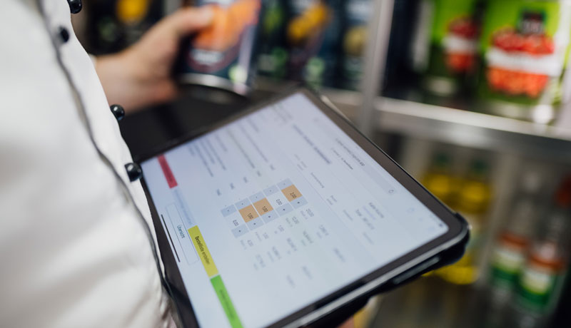 Koch im Warenlager mit Ipad, auf dem die App StockControl zu sehen ist